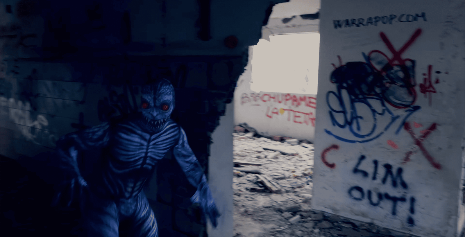 La criatura del videoclip de Bring The Madness sobre un fondo de escenario